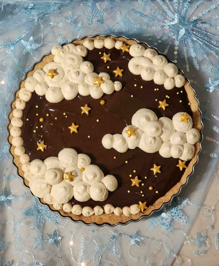 A rich chocolate tart topped with dreamy cloud and star designs, showcasing baking brilliance.