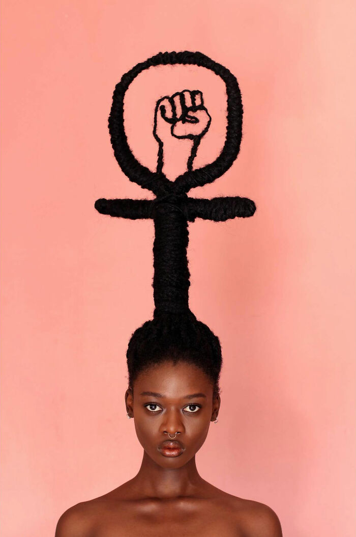 Woman with hair sculpted into a raised fist, symbolizing empowerment, against a peach background.