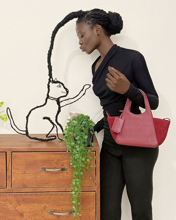 Hair-sculpture of a cat next to a wooden dresser, paired with a vibrant red bag.