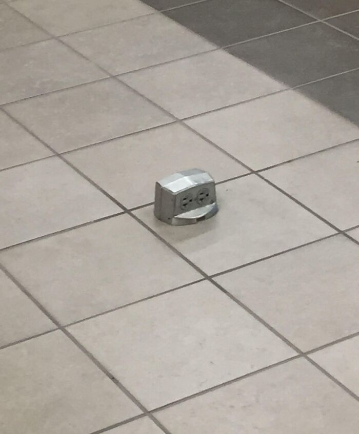 Floor electrical outlet installed in the middle of tiled walkway presenting a dangerous design and potential death trap hazard.