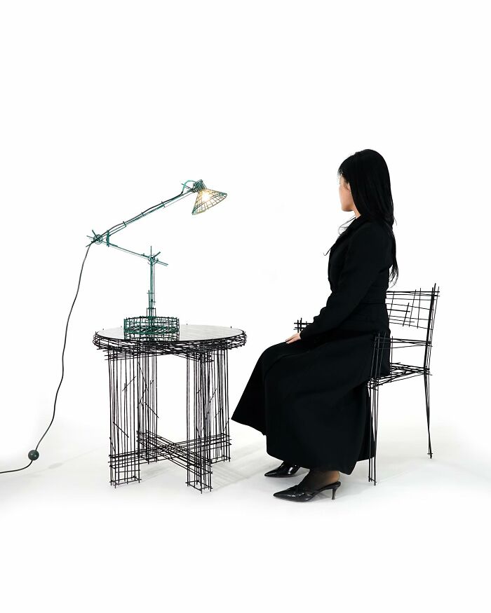 Woman sitting on doodle-style wireframe chair beside wireframe table and lamp, showcasing furniture pieces that look like doodles.