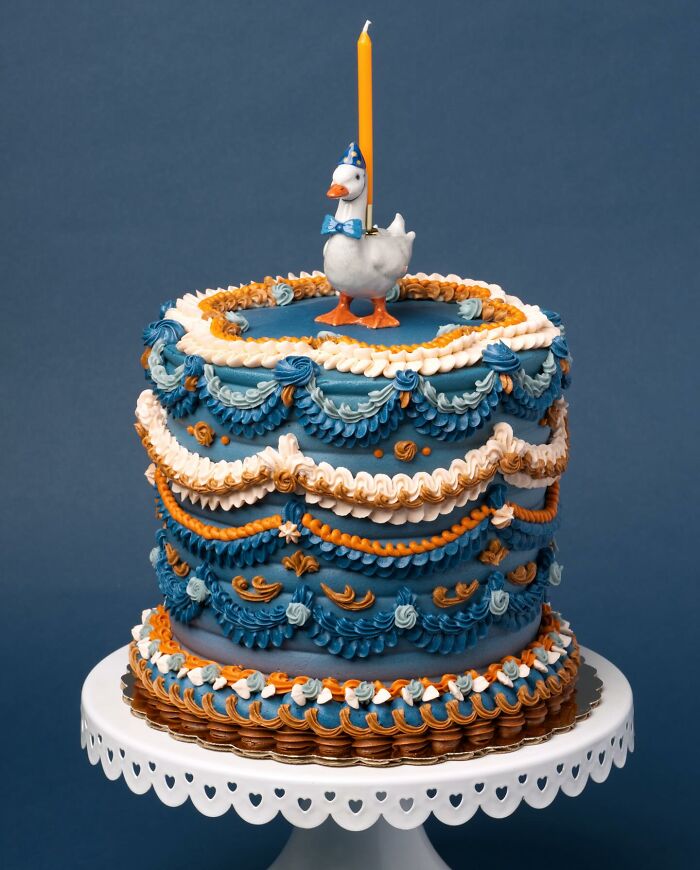 A playful vegan cake bursting with blue and orange frosting, topped with a cute duck figurine.