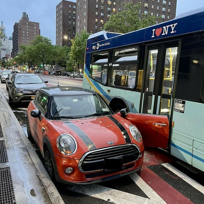 Red Mini Cooper with open driver door stuck next to a New York City bus, an unexpected fail causing a traffic disruption.