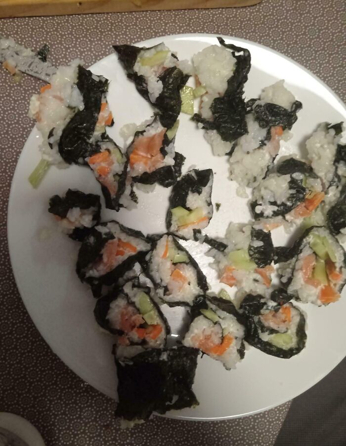 A poorly rolled sushi roll with rice spilling out on a white plate, a funny kitchen fail.