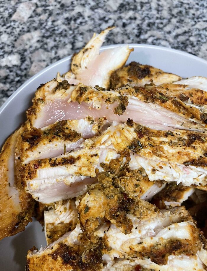 Undercooked chicken with pink, raw spots on a white plate against a sleek granite countertop.