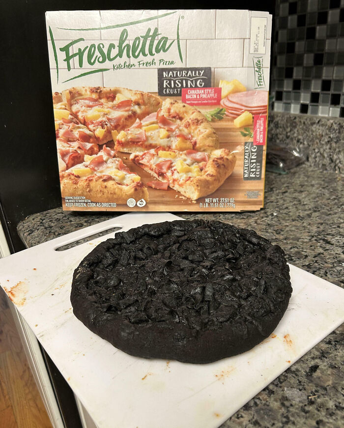 A burnt frozen pizza with a crispy, blackened crust on a cutting board in a cozy kitchen.