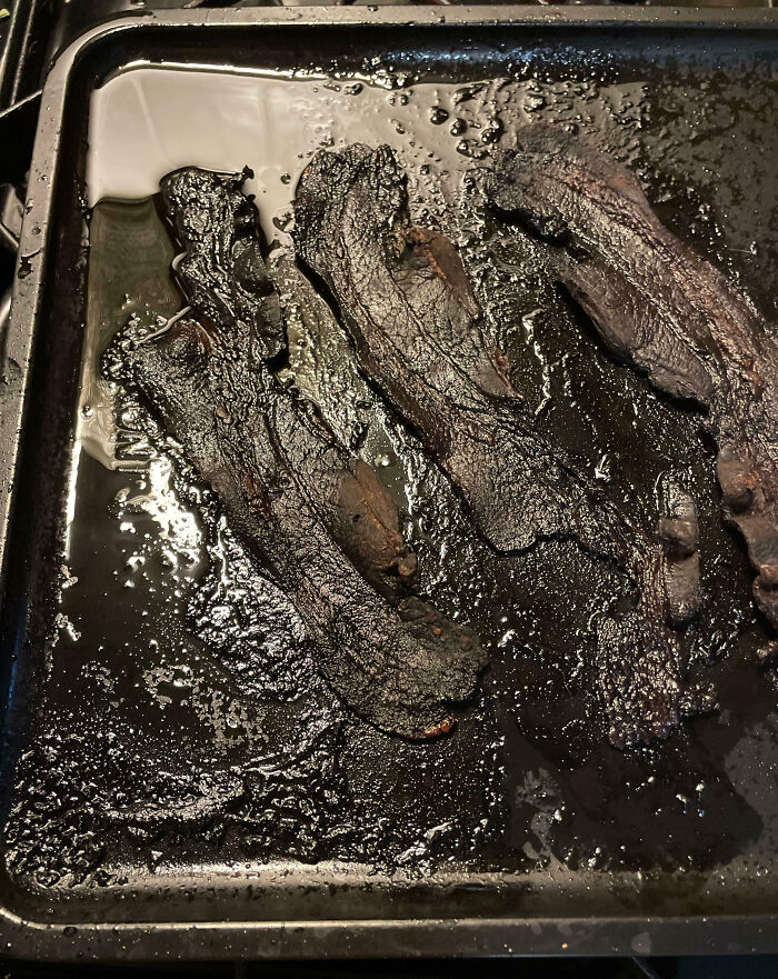 Burnt bacon slices on a shiny, greasy baking tray, a classic kitchen mishap.