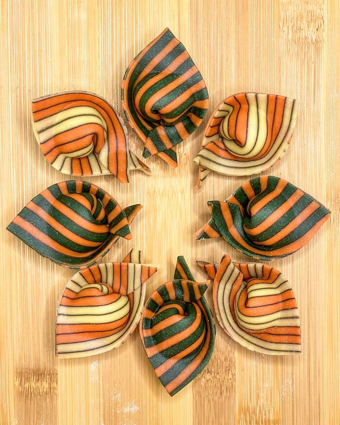 Colorful handcrafted pasta with orange, green, and cream stripes, arranged in a circular pattern on a wooden surface. Colorful handcrafted pasta with orange, green, and cream stripes, arranged in a circular pattern on a wooden surface.