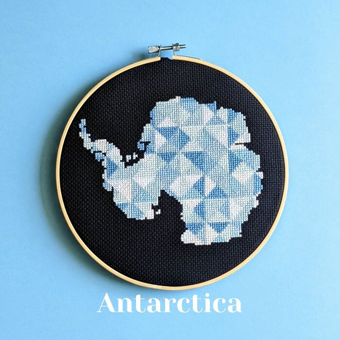 Antarctica’s map in cool blues and whites, stitched on black fabric and framed in a wooden hoop.
