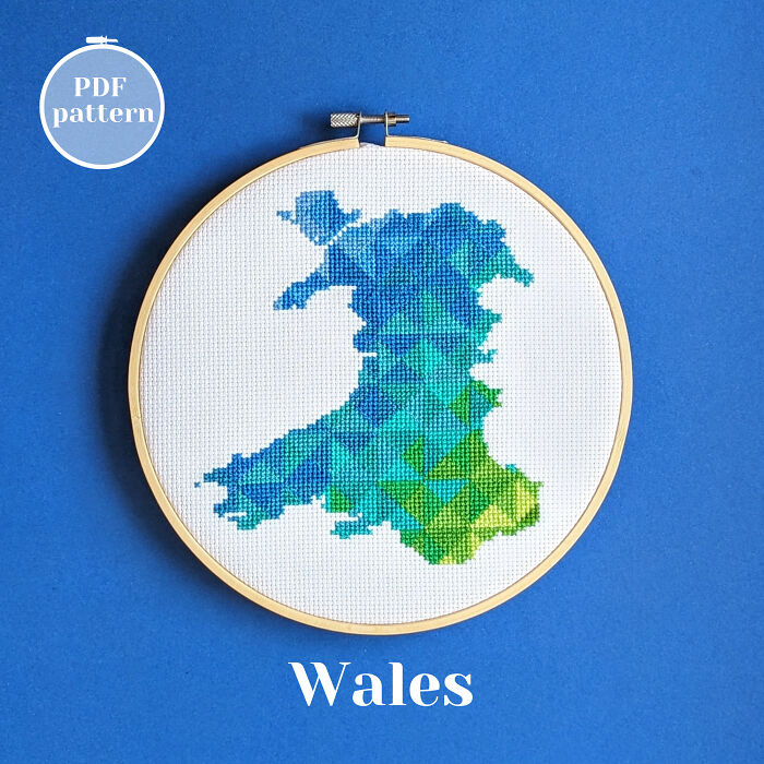 Wales’ map in geometric blues and greens, stitched with care and framed in a hoop on a blue background.
