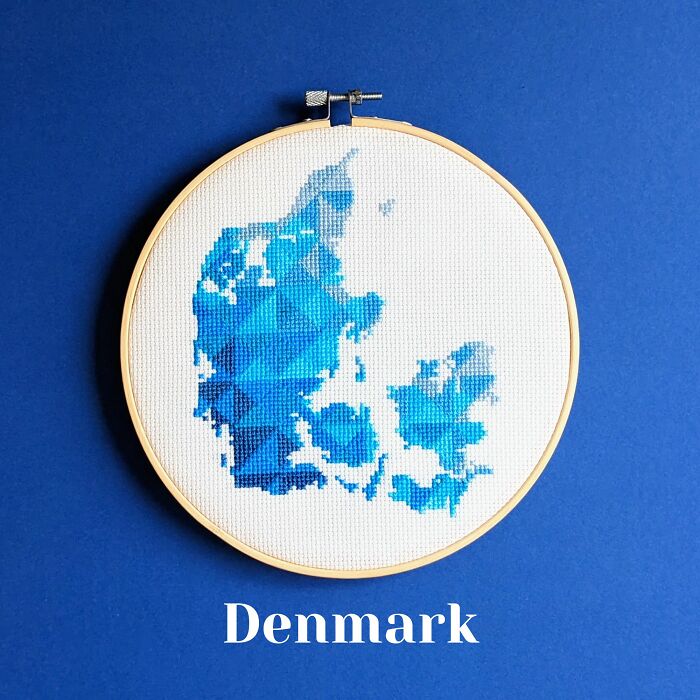 Denmark’s map in soft blues, stitched with precision and framed in a hoop on a calming blue background.