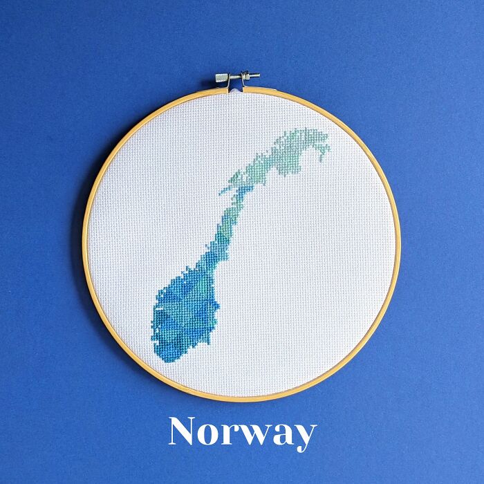 Norway’s map in cool blues and greens, stitched with care and framed in a wooden hoop on a calming blue background.