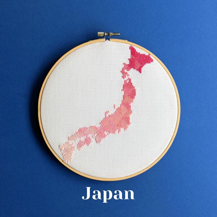 Japan’s map in soft pinks and reds, delicately stitched and framed in a hoop on a serene blue background.