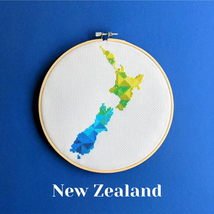 New Zealand’s map in bold geometric patterns, stitched with color and framed in a hoop on a blue background.