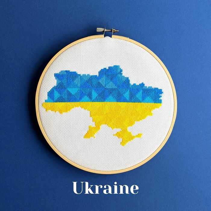 Vibrant cross-stitched map of Ukraine in bold blue and yellow, framed in a wooden hoop against a soothing blue backdrop.