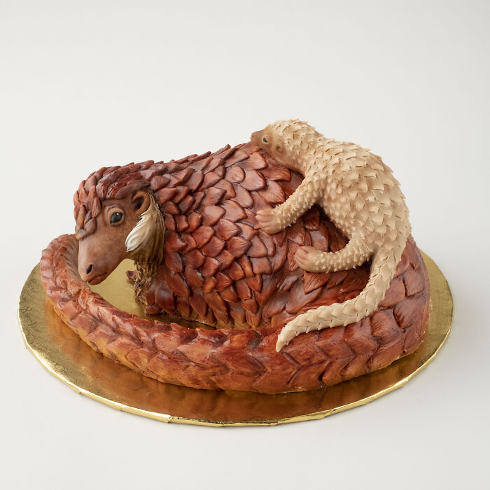 A vegan cake shaped like a pangolin, complete with detailed scales and a tiny baby on its back.